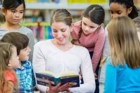 Grade school children listening to adult read a book