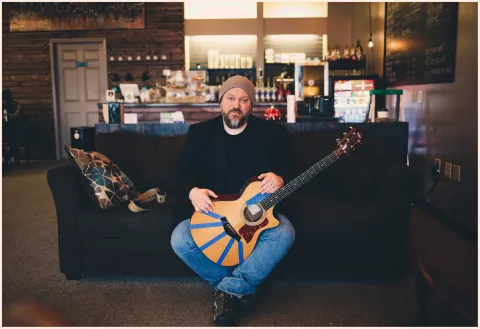 Some Guy Like Robb seated on a couch holding a guitar