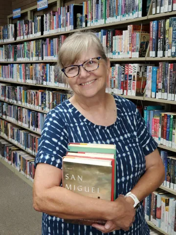 Ellen McWhirter holding a stack of books in a library