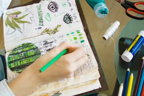 Hand writing in a journal plus craft supplies on table