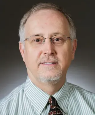 Professional headshot of Dr Peter Dykema, a grey haired man with glasses and wearing a dark tie