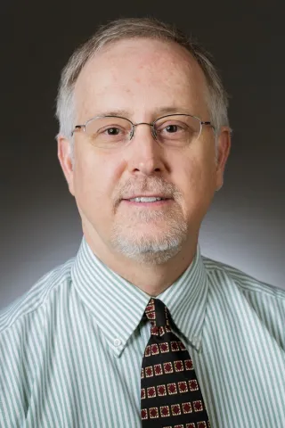 Professional headshot of Dr Peter Dykema, a grey haired man with glasses and wearing a dark tie