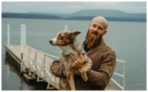 Photo of Eli Cranor on dock holding merle dog
