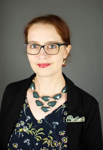 White woman standing in front of a grey background wearing a necklace of blue stones