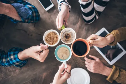 4 hands holding 4 cups of coffee in the center of a table