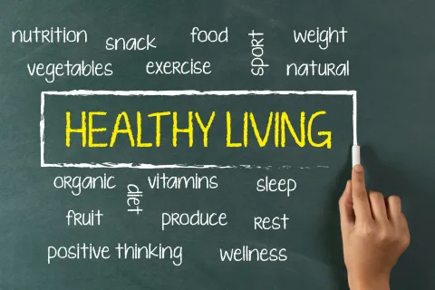 The word "Healthy Living" on chalk board with hand holding chalk surrounded by other words relating to health