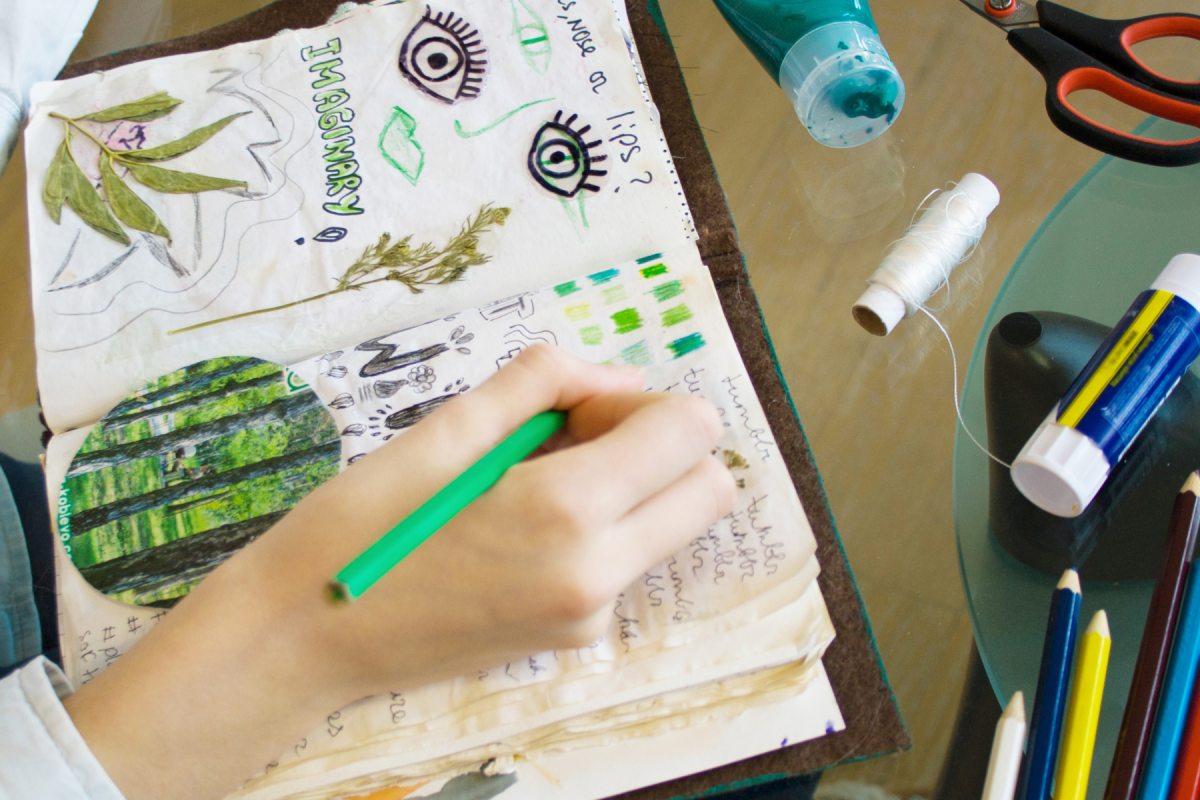 Hand writing in a journal plus craft supplies on table