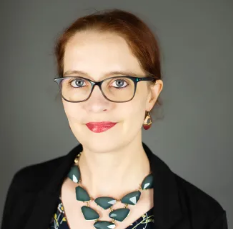 White woman standing in front of a grey background wearing a necklace of blue stones
