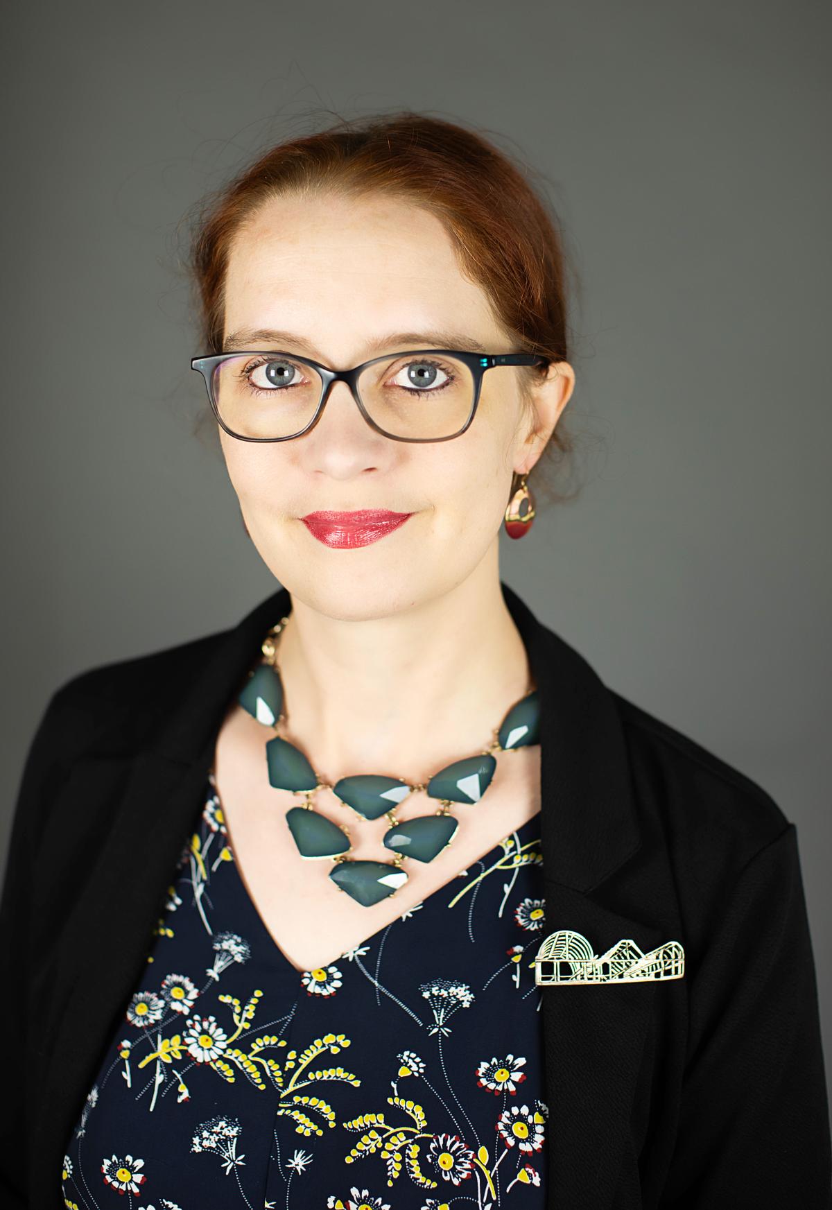 White woman standing in front of a grey background wearing a necklace of blue stones